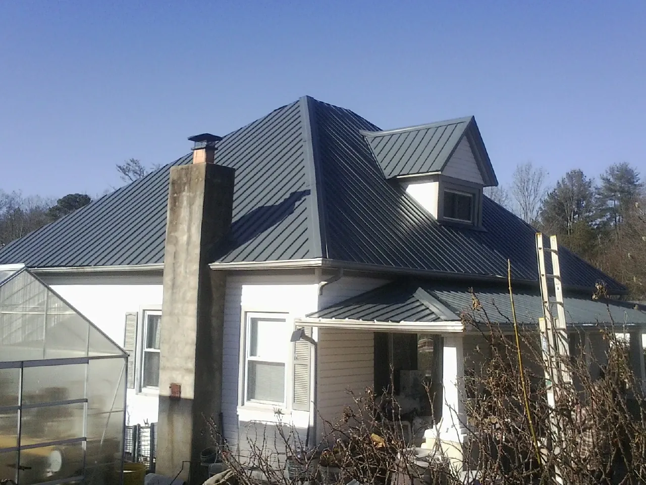 Dark blue standing seam metal roof on a white farmhouse with dormer — Slate & Tile Roof Repair by Roofing Brothers in Sabine Pass
