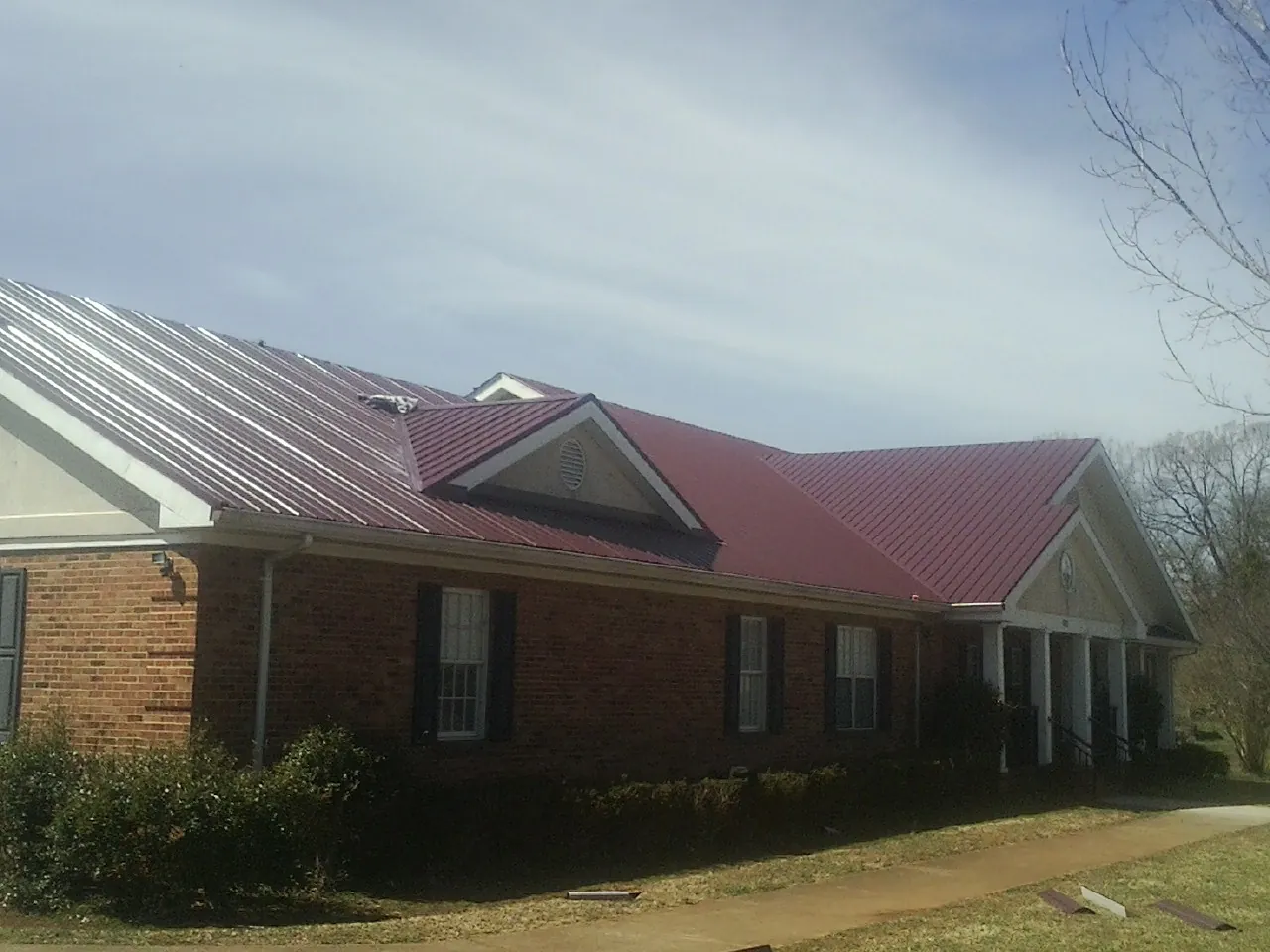 Red metal roof with gabled entries on a long brick building, from a Hail Damage Roof Repair job in Sabine Pass