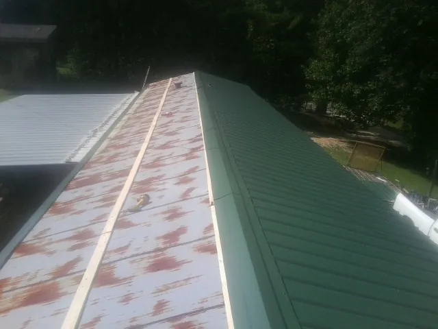 Old rusted panels beside newly installed green metal roofing — Wind Damage Roof Repair by Roofing Brothers in Sabine Pass