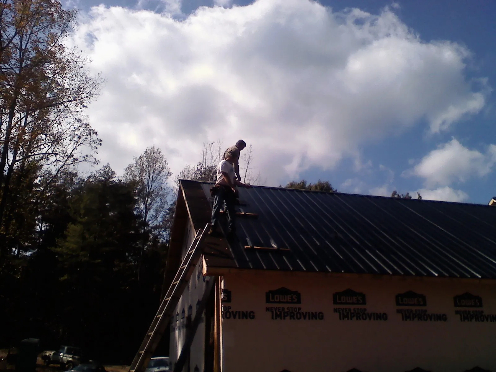 Roofer fastening dark metal panels high against a cloudy sky, from a Roof Inspection job in Sabine Pass
