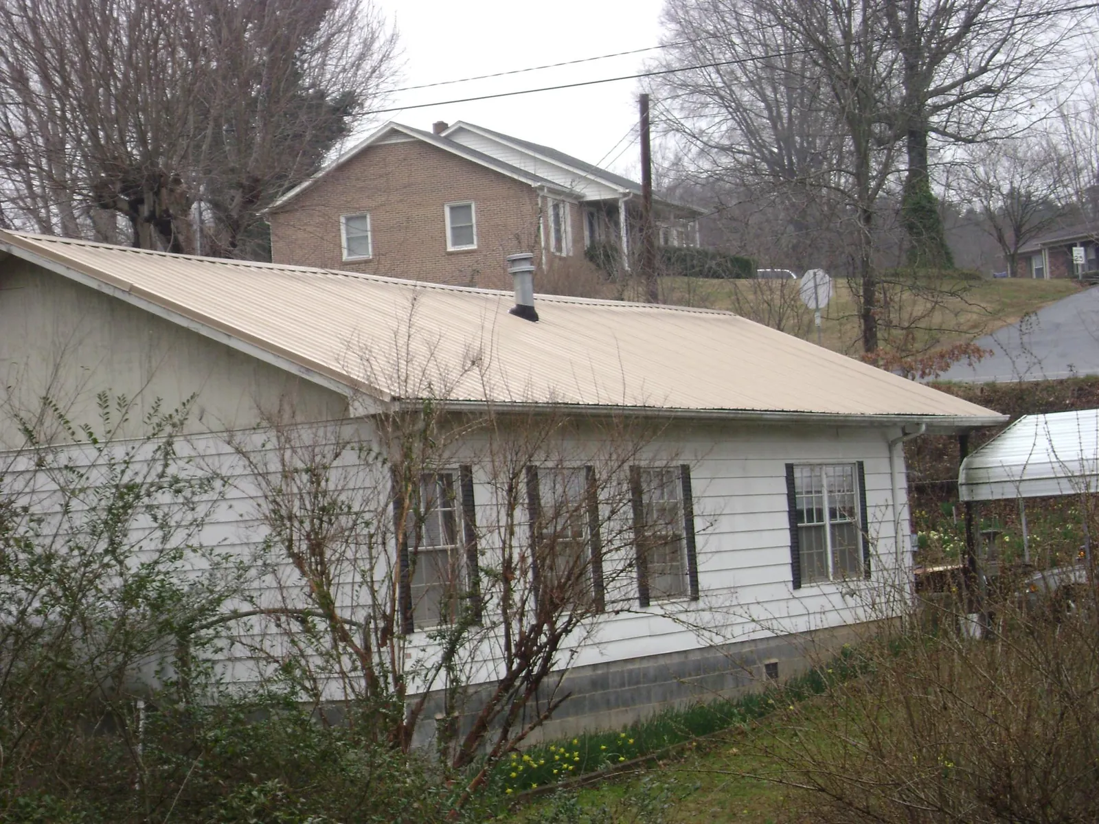 Tan metal roof on a white sided house set into a hillside — Commercial Roofing by Roofing Brothers in Sabine Pass